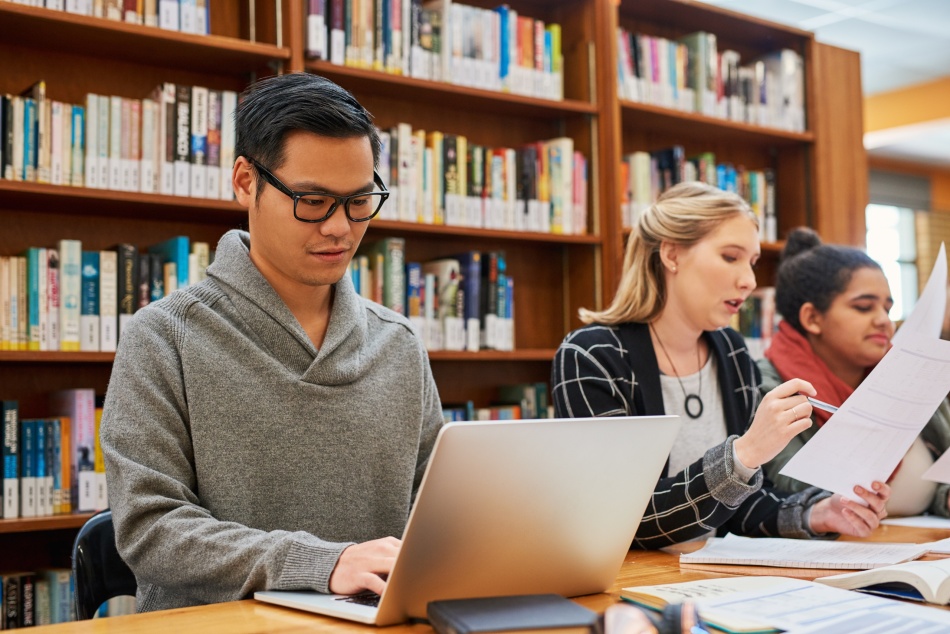Laptop, typing and man in library for study with university, education and scholarship for growth. Books, online research and college student on campus with learning, knowledge and writing paper.