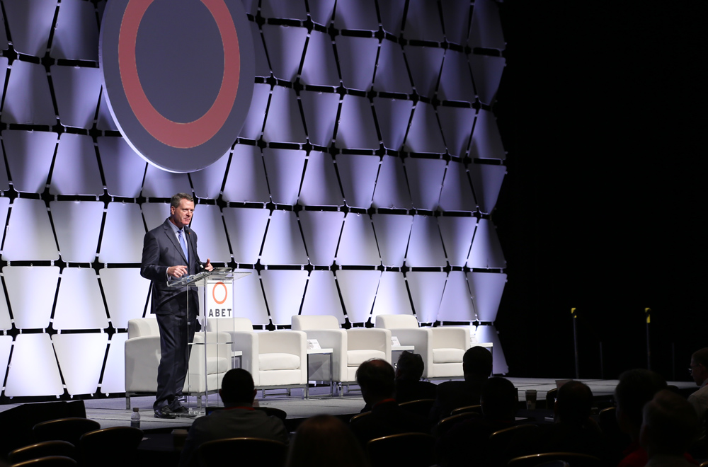 ABET’s CEO Michael Milligan stands on stage addressing an audience behind a podium with the ABET logo.