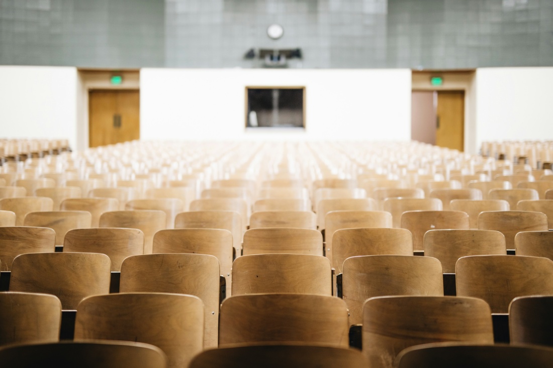 Empty lecture hall with rows of wooden auditorium seats facing the front of the room.